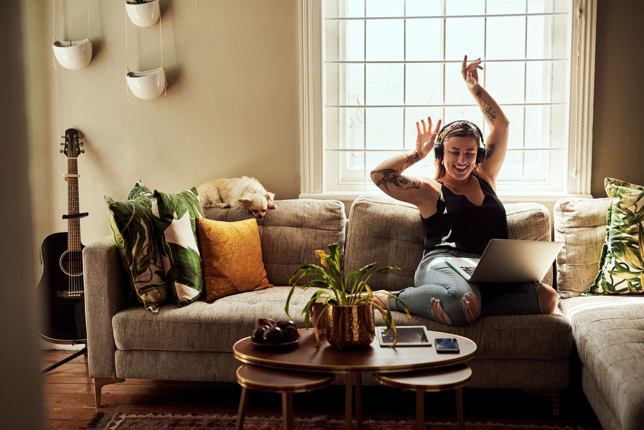 Shot of a young woman using a laptop and headphones on the sofa at home