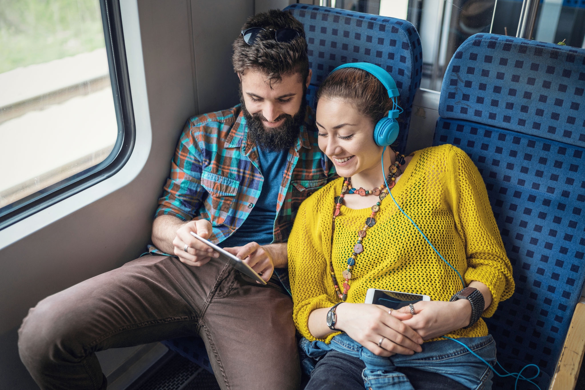 Attractive happy couple listening to music and browsing on the tablet while travelling